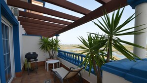En balkon med et bord, stole, grill og krukker med planter.