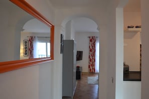 Ein Flur mit einer Spiegelwand, einem Kühlschrank, einem Fernseher und einer Tür zu einem Zimmer mit Fenster und Vorhängen.