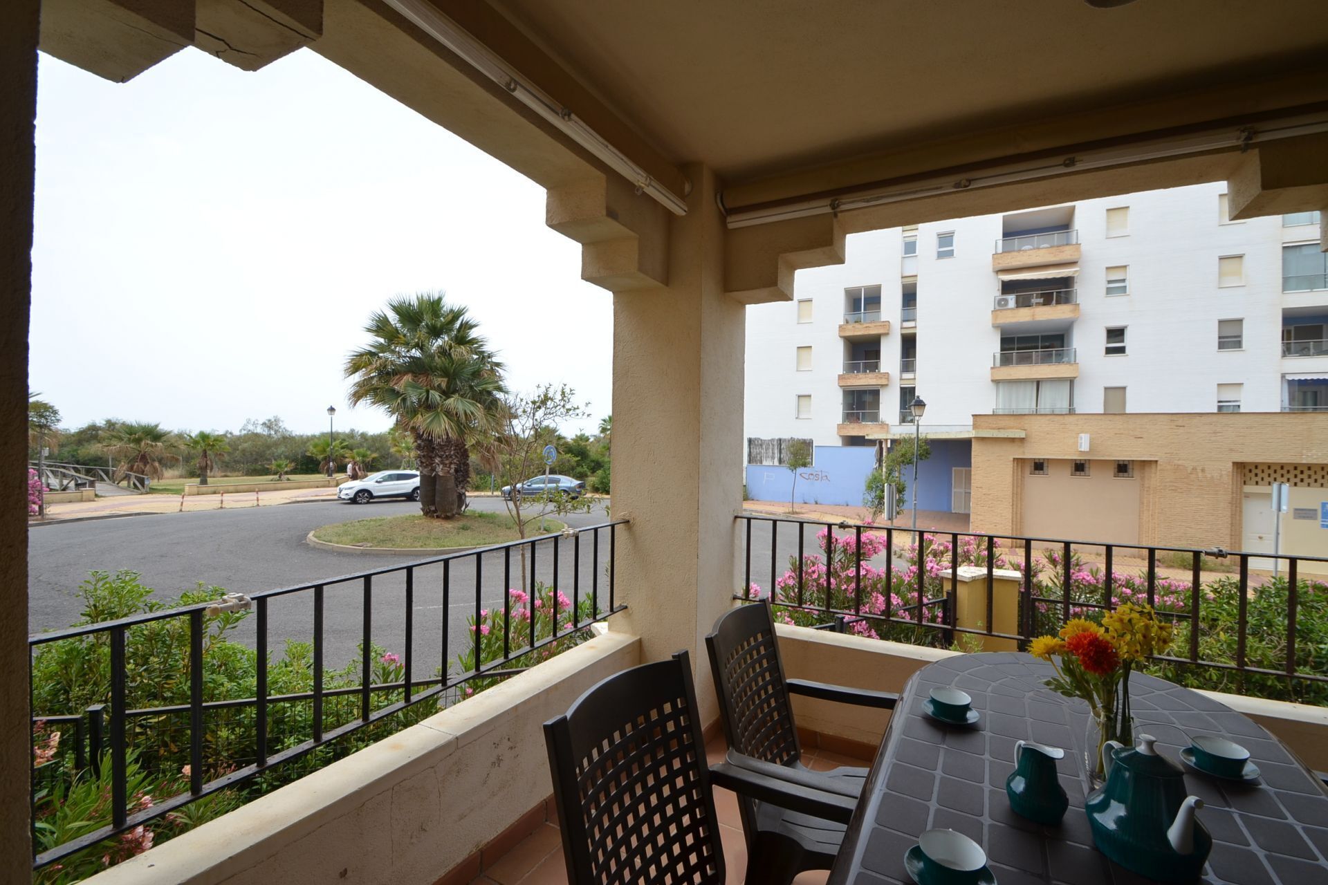 Varanda com mesa posta para chá, com vista para uma rua com carros e uma palmeira.