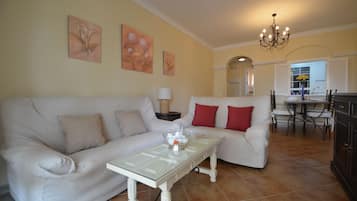Uma sala de estar com um sofá branco, uma mesa de centro de vidro e um candelabro.