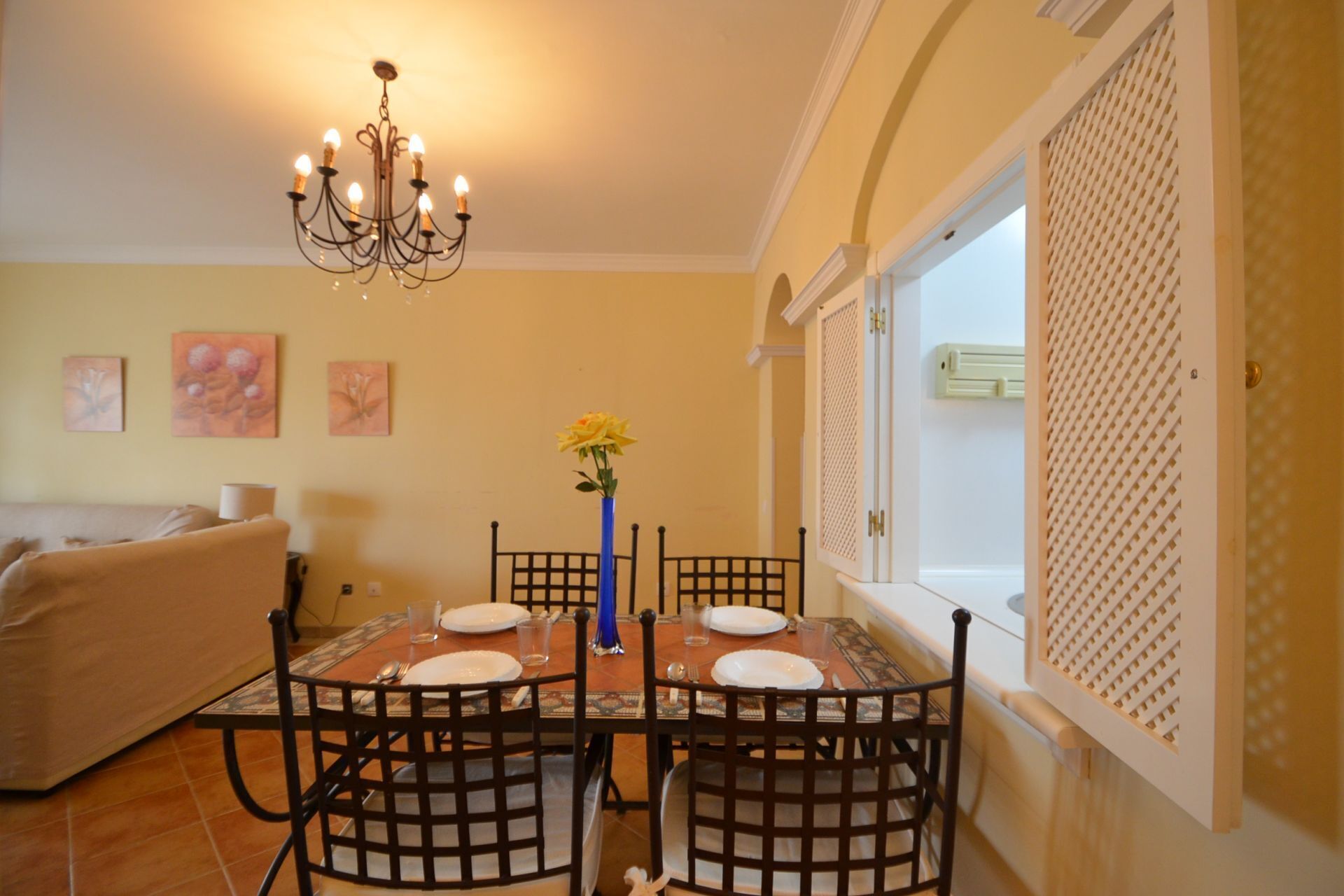 Un coin repas avec une table dressée pour quatre personnes, entourée de chaises, d’un lustre et de deux tableaux accrochés au mur.