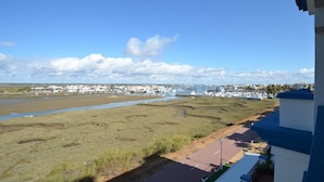 A coastal view with a marina, grassy areas, and a road leading to a building with a blue roof. - LA MARINA 3 21 - Two Bedroom Apartment, Sleeps 5 (Punta del moral)