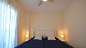 A double bed with a white headboard, two bedside lamps, and a ceiling fan.