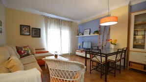 Un salon avec un canapé, une table à manger et des chaises, un panier en osier et un téléviseur.