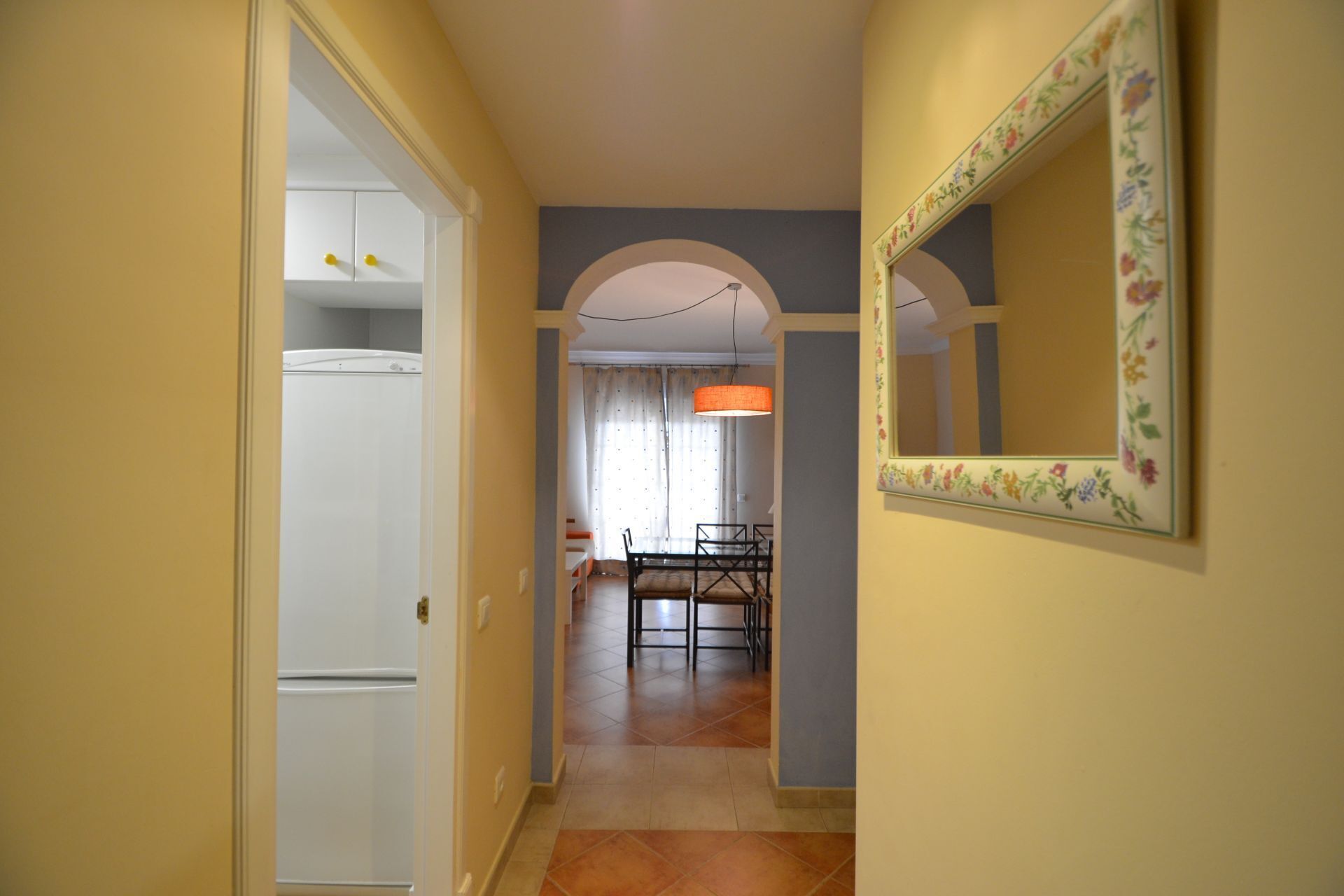 A hallway with a dining area, a mirror with a floral frame, and a ceiling light.