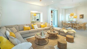 A modern living room with a sectional sofa, round coffee tables, and wicker ottomans. - Stunning Seafront Villa in the Mondragó National Park, Amazing Views & Direct Access to the Beach! (Cala Mondrago)