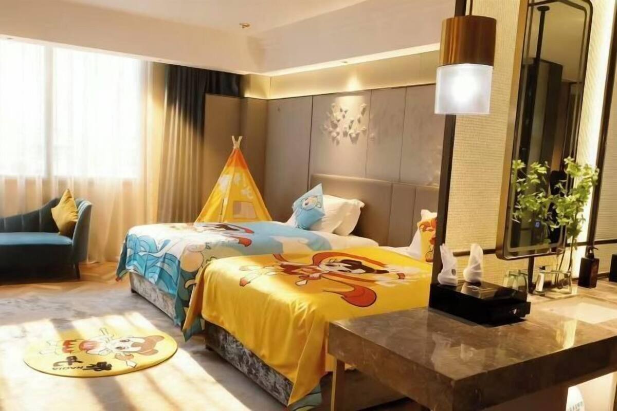 Habitación de hotel con cama, mesita de noche, espejo, ventana con cortinas y una alfombra redonda pequeña.