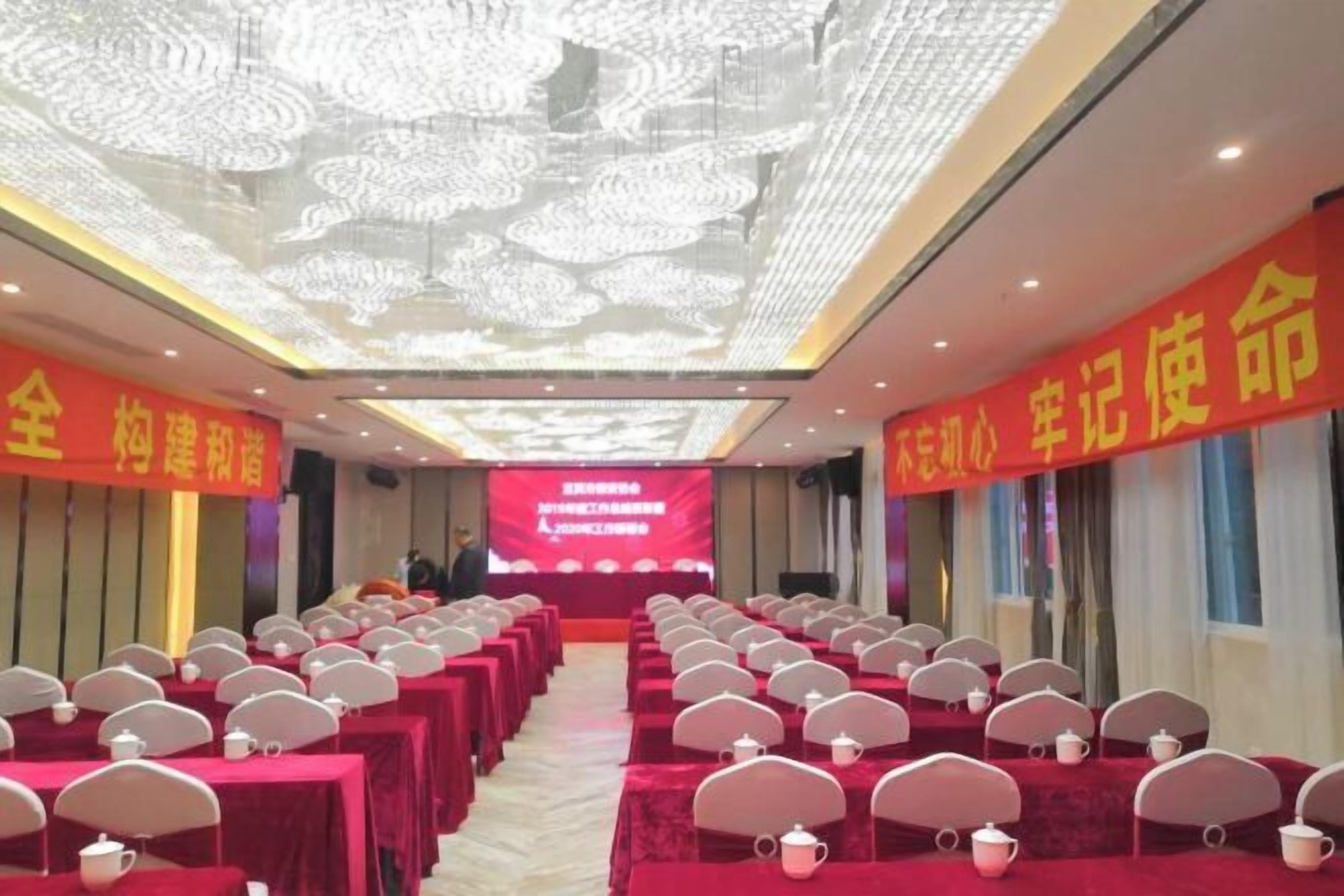 A conference room with rows of tables and chairs, a large screen at the front, and red banners on the walls.