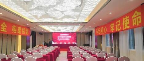 A conference room with rows of tables and chairs, a large screen at the front, and red banners on the walls.