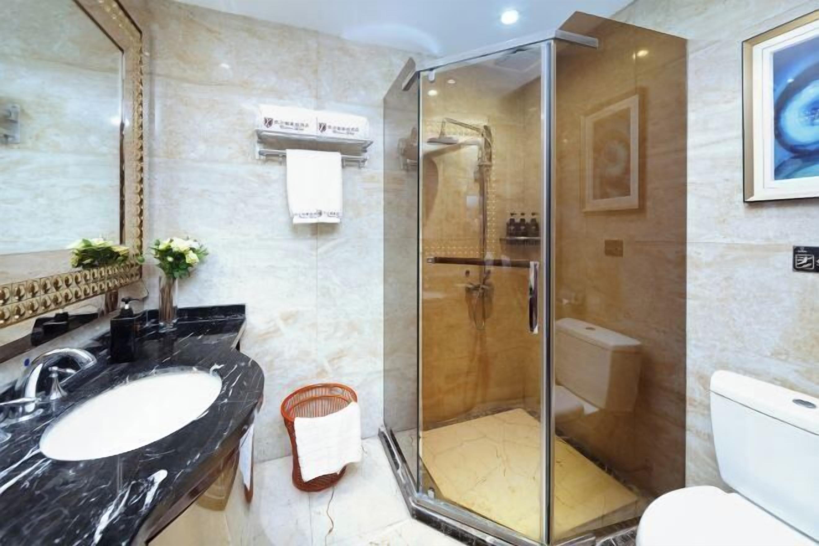 Een badkamer met een marmeren wastafel, een douche met glazen wanden en een toilet.