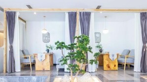Una zona de recepción con mostradores de madera, cortinas grises y una planta central.