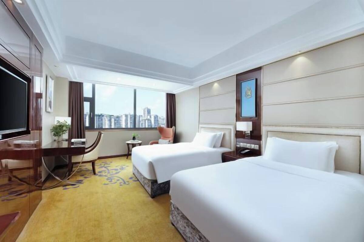 Habitación de hotel con dos camas, un escritorio, televisión y vista a la ciudad.