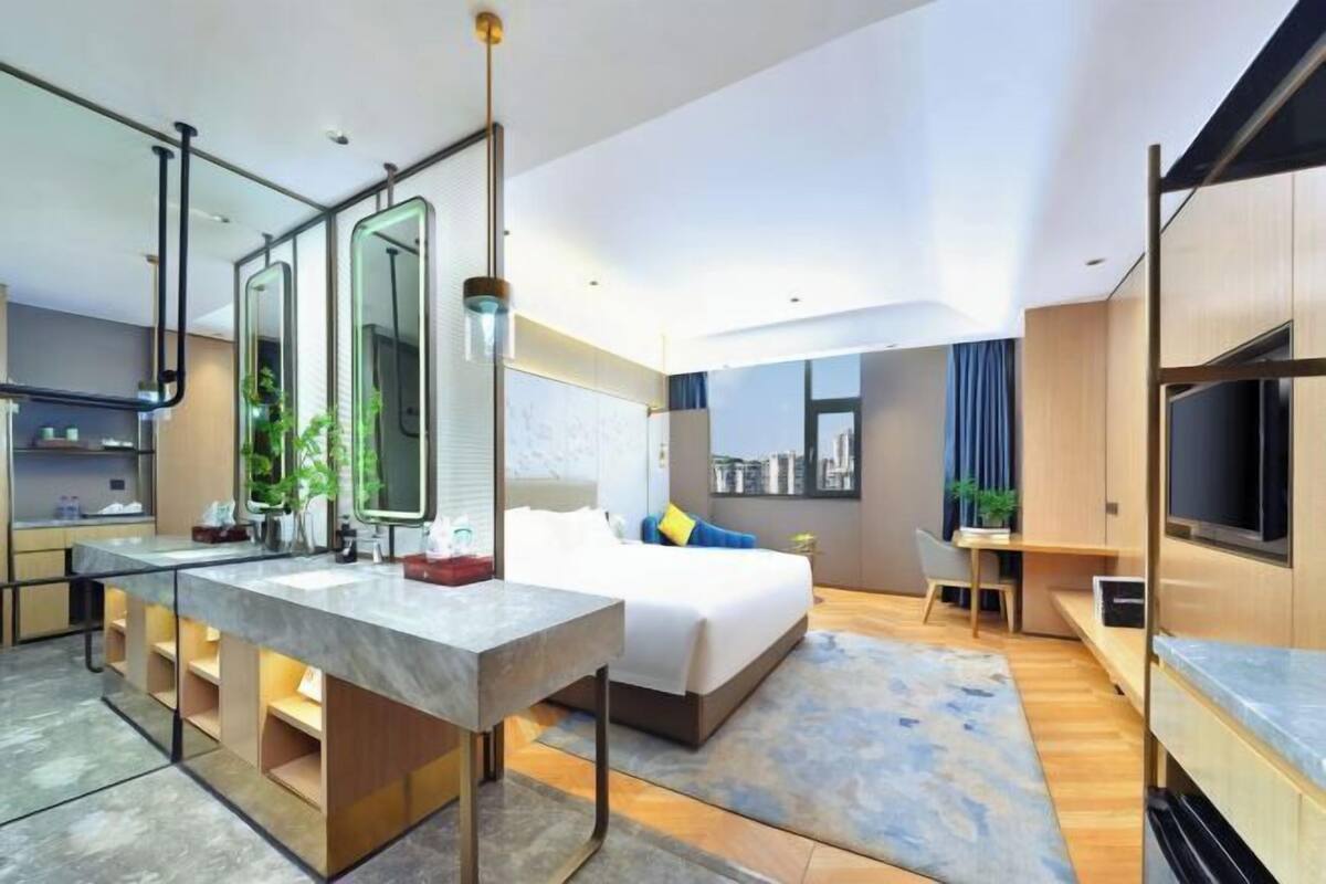 Una habitación de hotel moderna con una cama grande, un escritorio, un televisor y un baño con un espejo amplio.