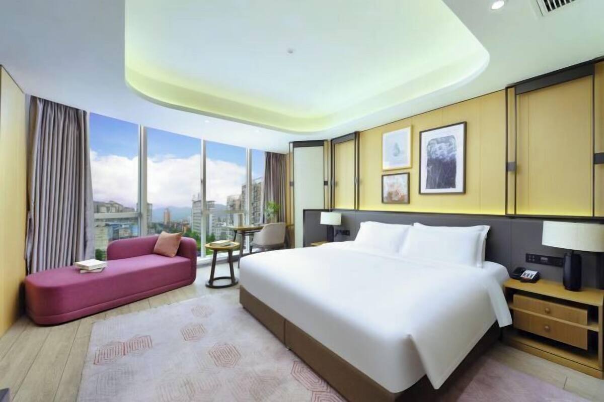 Habitación de hotel con una cama grande, un sofá, una mesita y vistas a la ciudad.