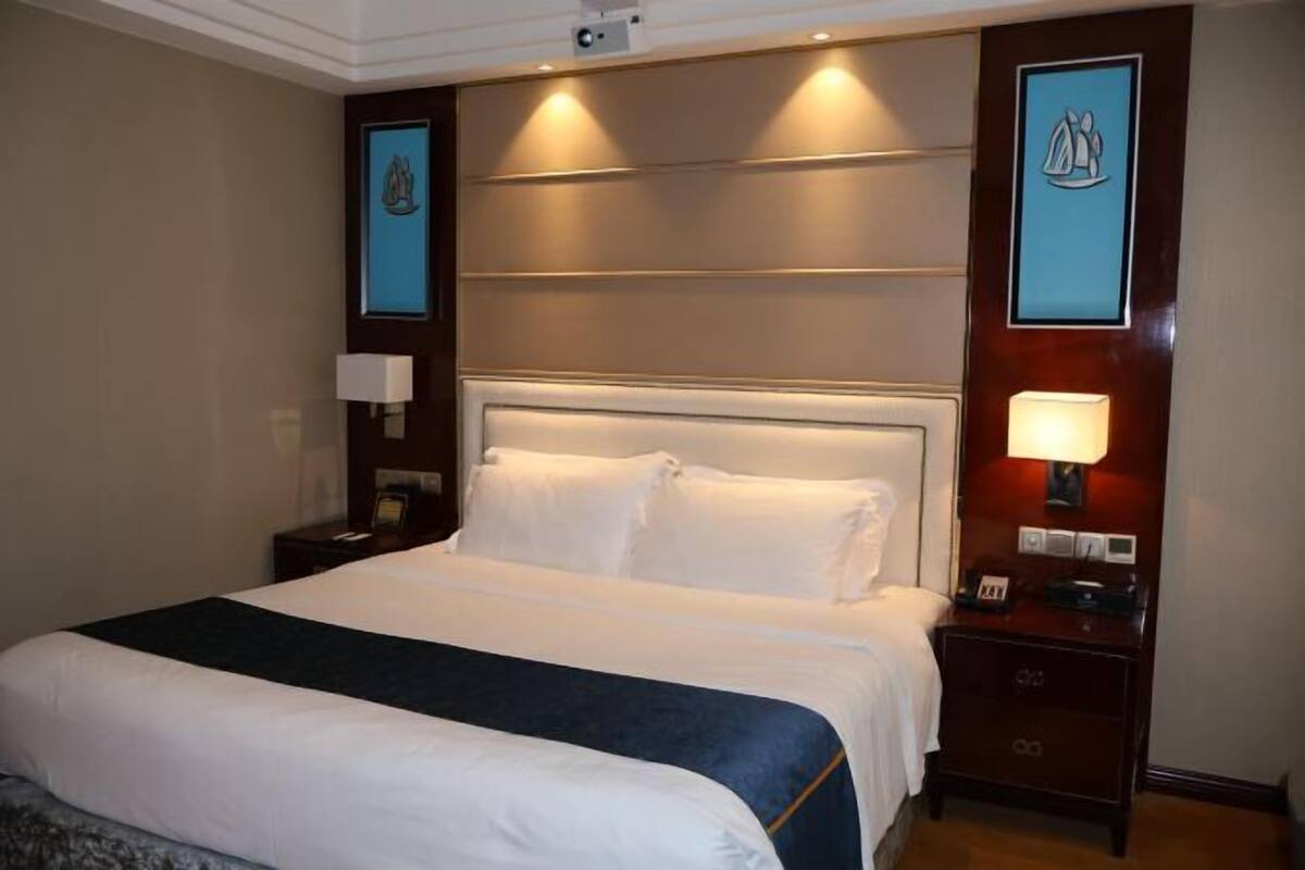 Habitación de hotel con una cama grande, lámparas de noche, una mesita de noche y un cuadro enmarcado en la pared.