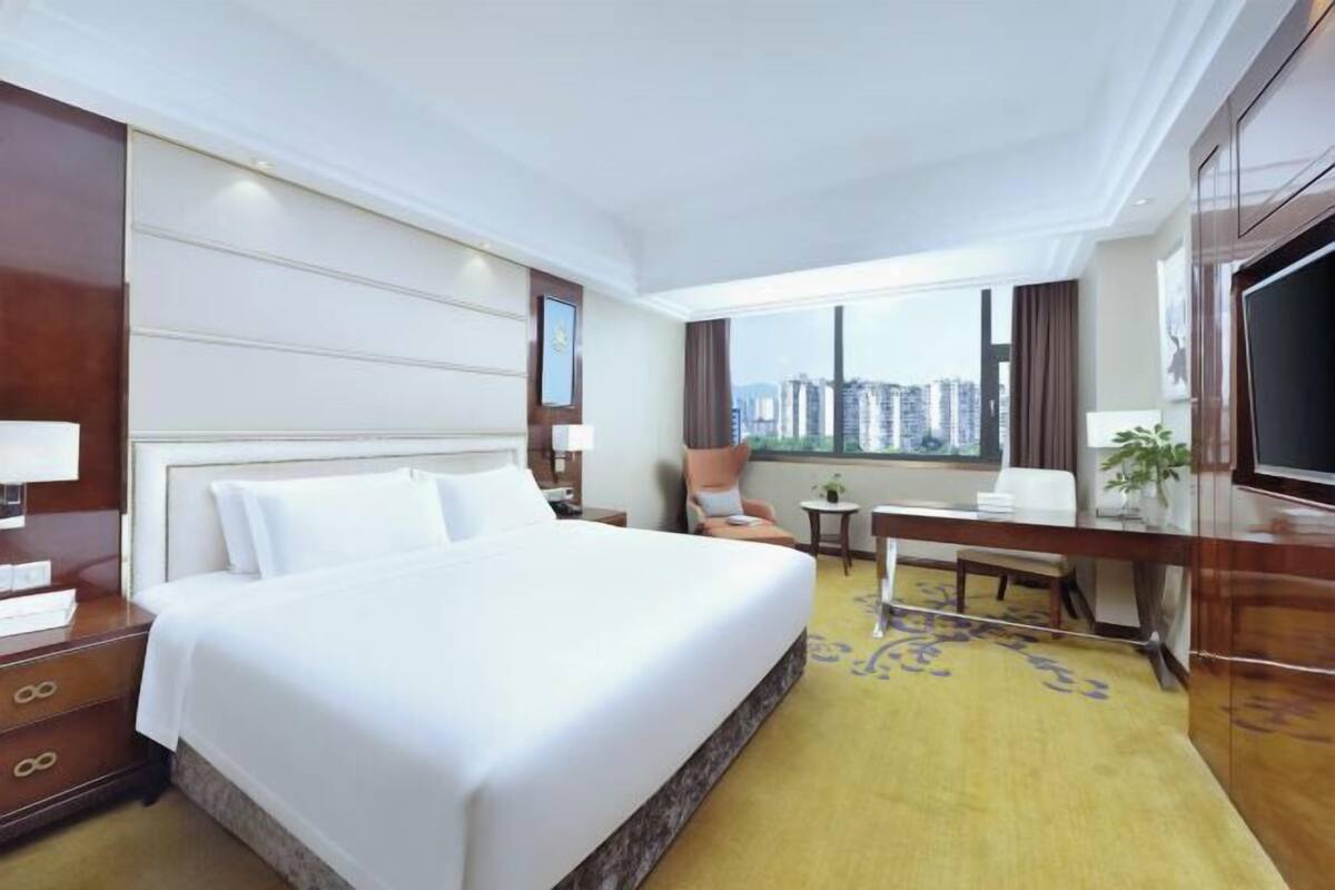 Habitación de hotel con una cama grande, un escritorio, una silla, un televisor y una ventana con vistas a la ciudad.