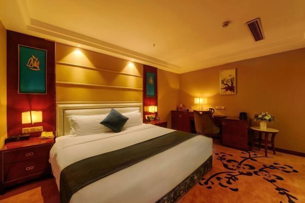 Habitación de hotel con una cama grande, un escritorio y una silla. Hay lámparas de pared y un cuadro en la pared.