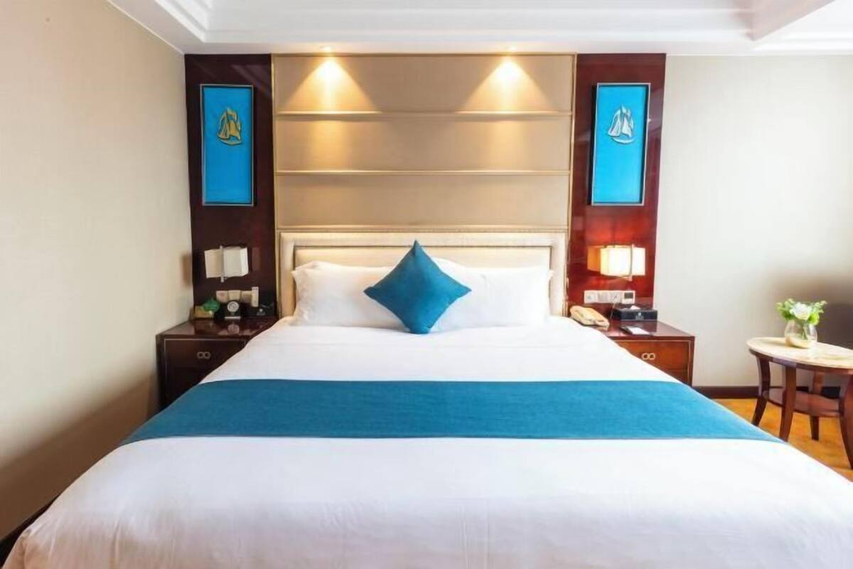 Una habitación de hotel con cama, mesitas de noche, lámparas y cuadros en la pared.