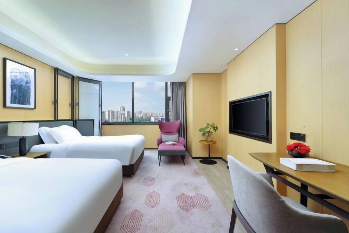 Habitación de hotel con dos camas, un escritorio, una silla, un televisor y vistas a la ciudad.
