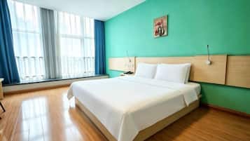A hotel room with a large bed, a nightstand, a window with curtains, and a green wall.