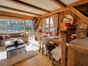 A cozy, wooden-furnished living room with a sofa, coffee table, and a dining area with a table set for four. - Le repaire du skieur Megève village (Megève)