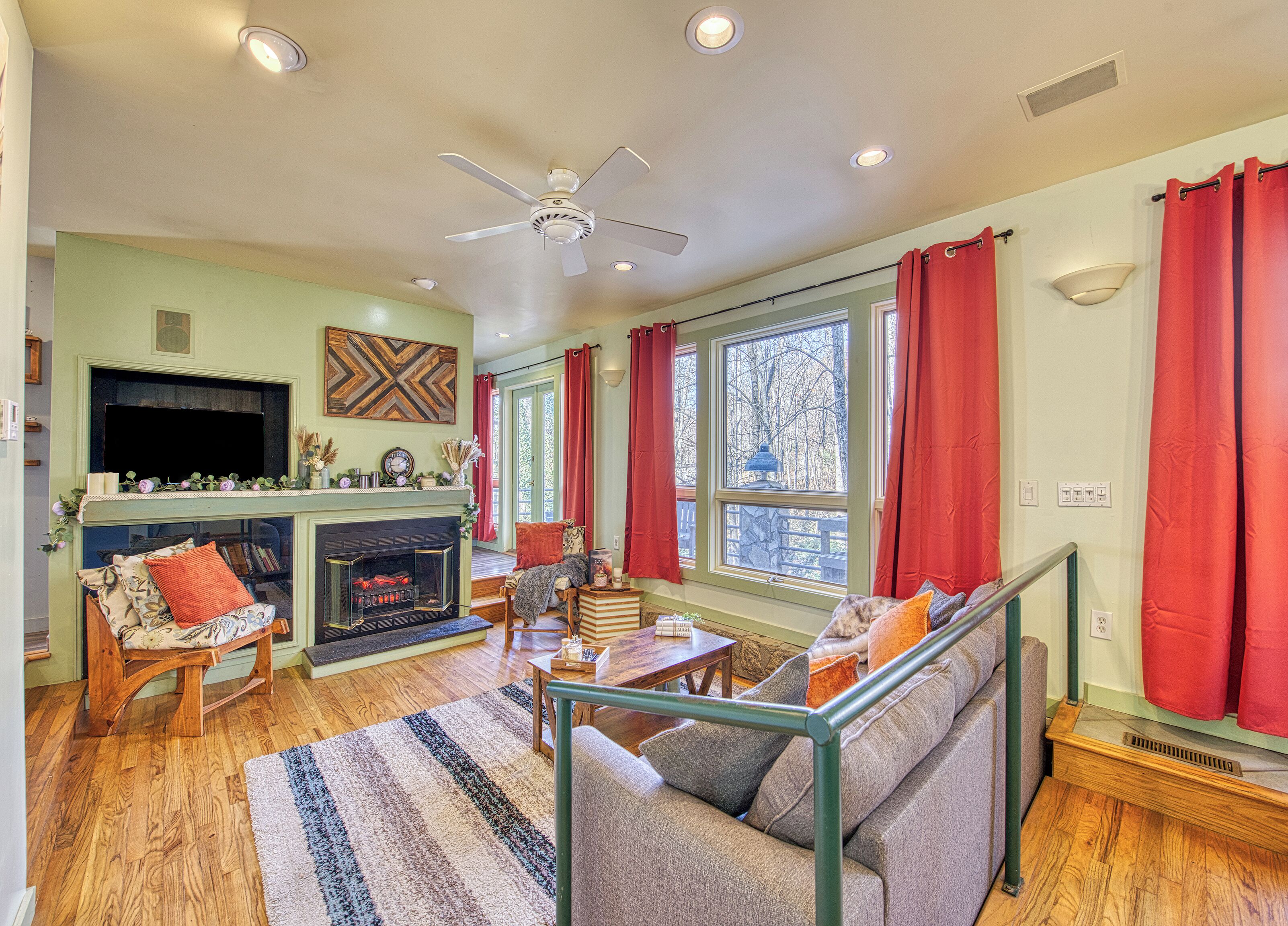 A cozy living room with a fireplace, a sofa, a television, and a large window with curtains.