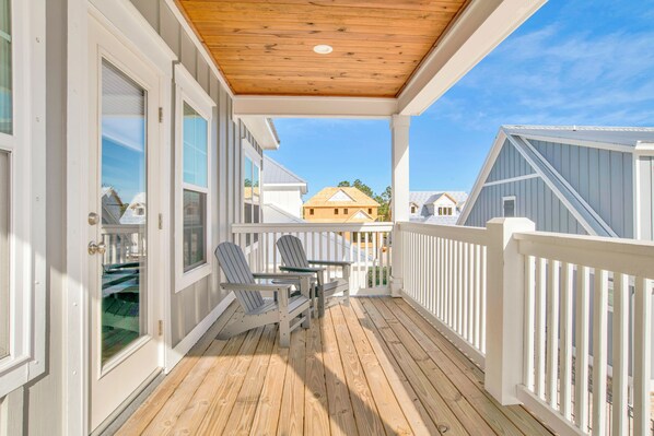 A wooden deck with a white railing, two Adirondack chairs, and a small table.