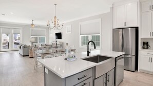 A modern kitchen with white cabinetry, a stainless steel refrigerator, and a central island with a sink. - Pool, Walk To Beach & Restaurants, Firepit, 4BR + Bunks, Summer Salt Amenities (Orange Beach)