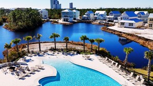 A resort with a large swimming pool, lounge chairs, and a view of a water body and buildings in the background. - Pool, Walk To Beach & Restaurants, Firepit, 4BR + Bunks, Summer Salt Amenities (Orange Beach)
