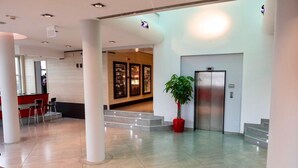 Un hall d’entrée moderne comprenant un comptoir d’accueil, un espace salon et un ascenseur.