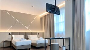 Une chambre d’hôtel moderne équipée de deux lits, d’un téléviseur à écran plat fixé au mur, d’une petite table et d’une poubelle.