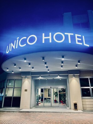 The exterior of the UNICO HOTEL with a prominent illuminated sign, large glass entrance, and a modern architectural design. - Unico Hotel (Ossona)