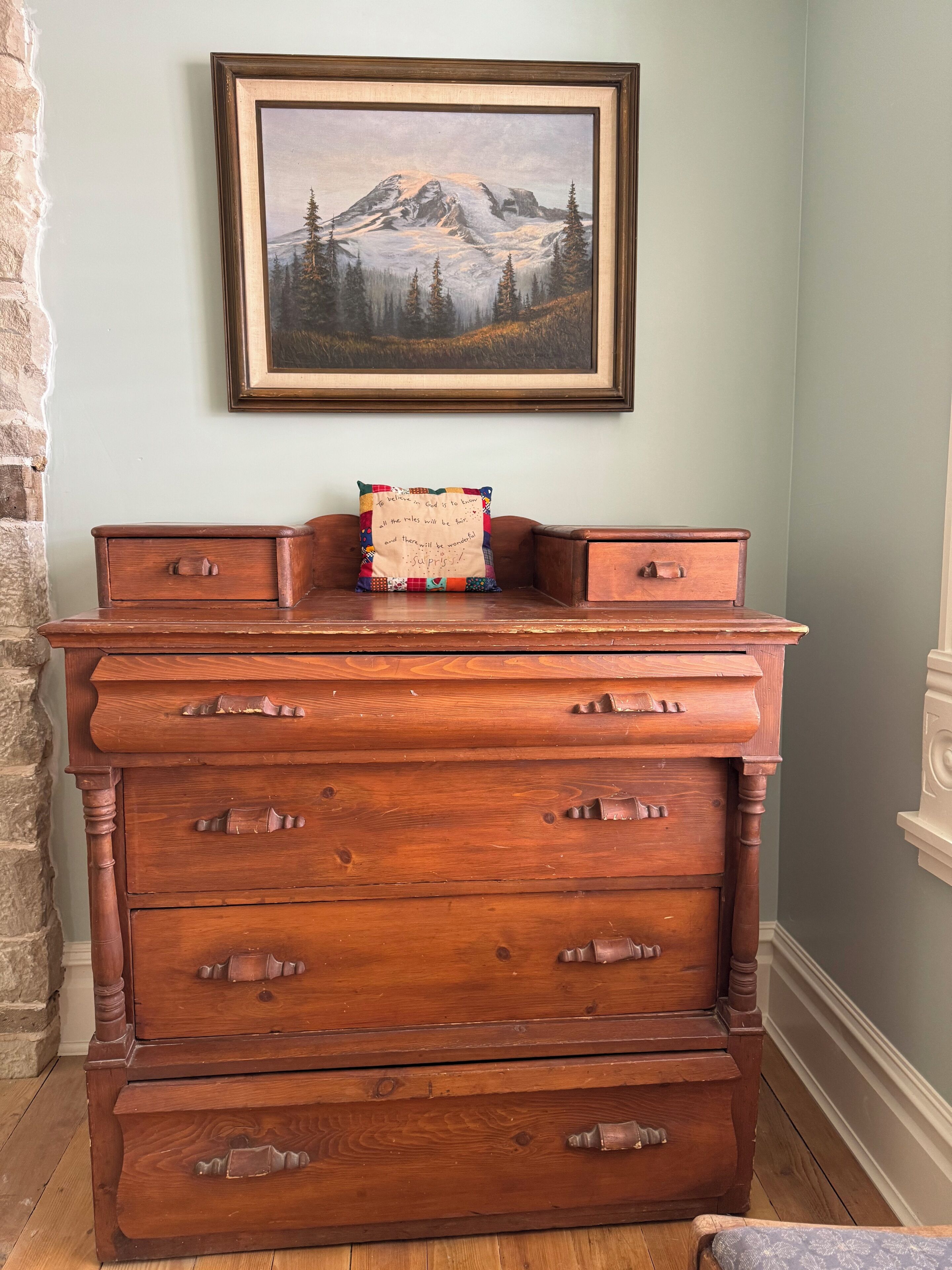 A wooden dresser with multiple drawers and a framed painting above it.
