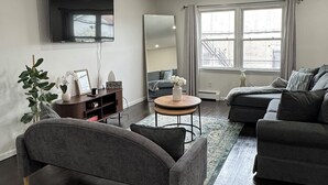 Un salon moderne avec un parquet en bois foncé, un canapé gris, une table basse ronde et un téléviseur à écran plat fixé au mur.