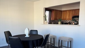 Un coin repas avec une table ronde, des chaises noires et un tapis à motifs. Une fenêtre se trouve au-dessus du comptoir, et des armoires en bois sont installées en hauteur.