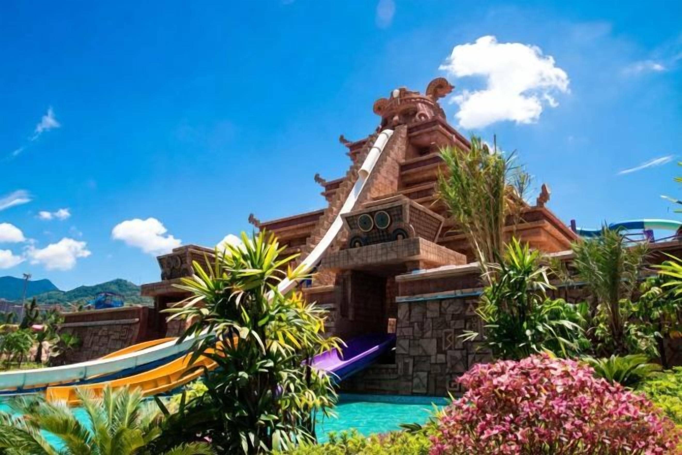 A water park with a large waterfall, slides, and a pool surrounded by tropical vegetation.