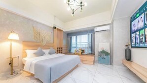 Ein modernes Hotelzimmer mit einem großen Bett, einer Nachttischlampe, einem Holzkopfende, einem an der Wand montierten Fernseher und einem großen Fenster mit Stadtblick.