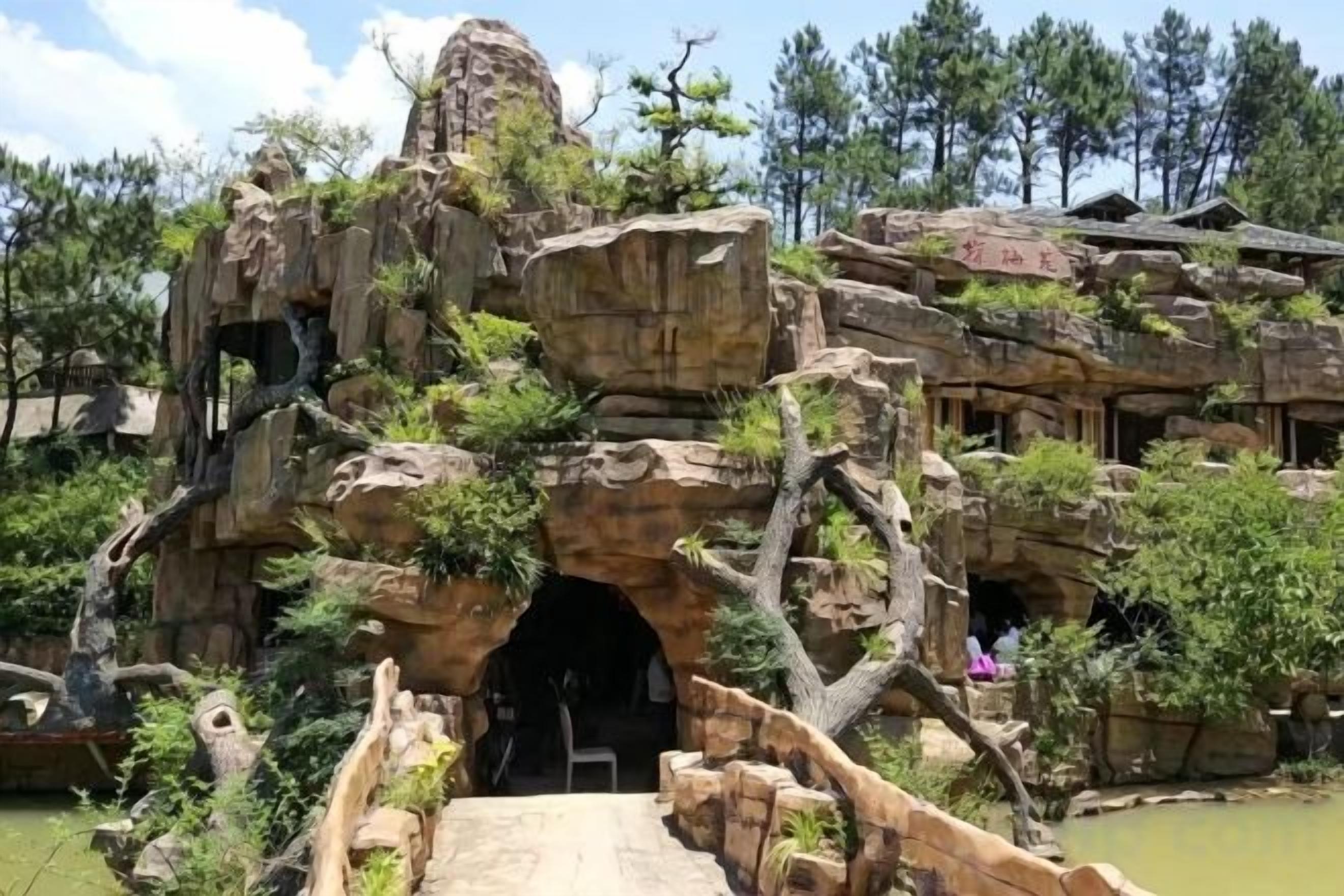 A naturalistic rock formation with an entrance tunnel, surrounded by trees and vegetation.