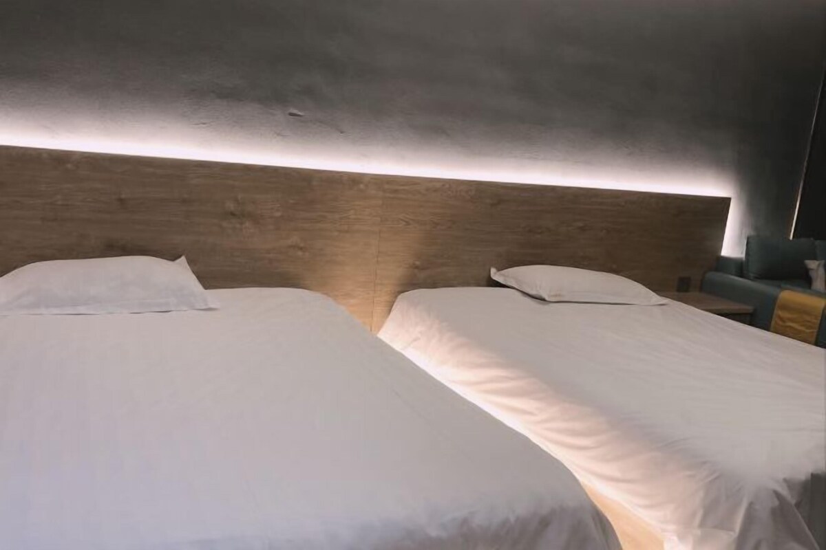A hotel room with two single beds, a wooden headboard, and a nightstand.