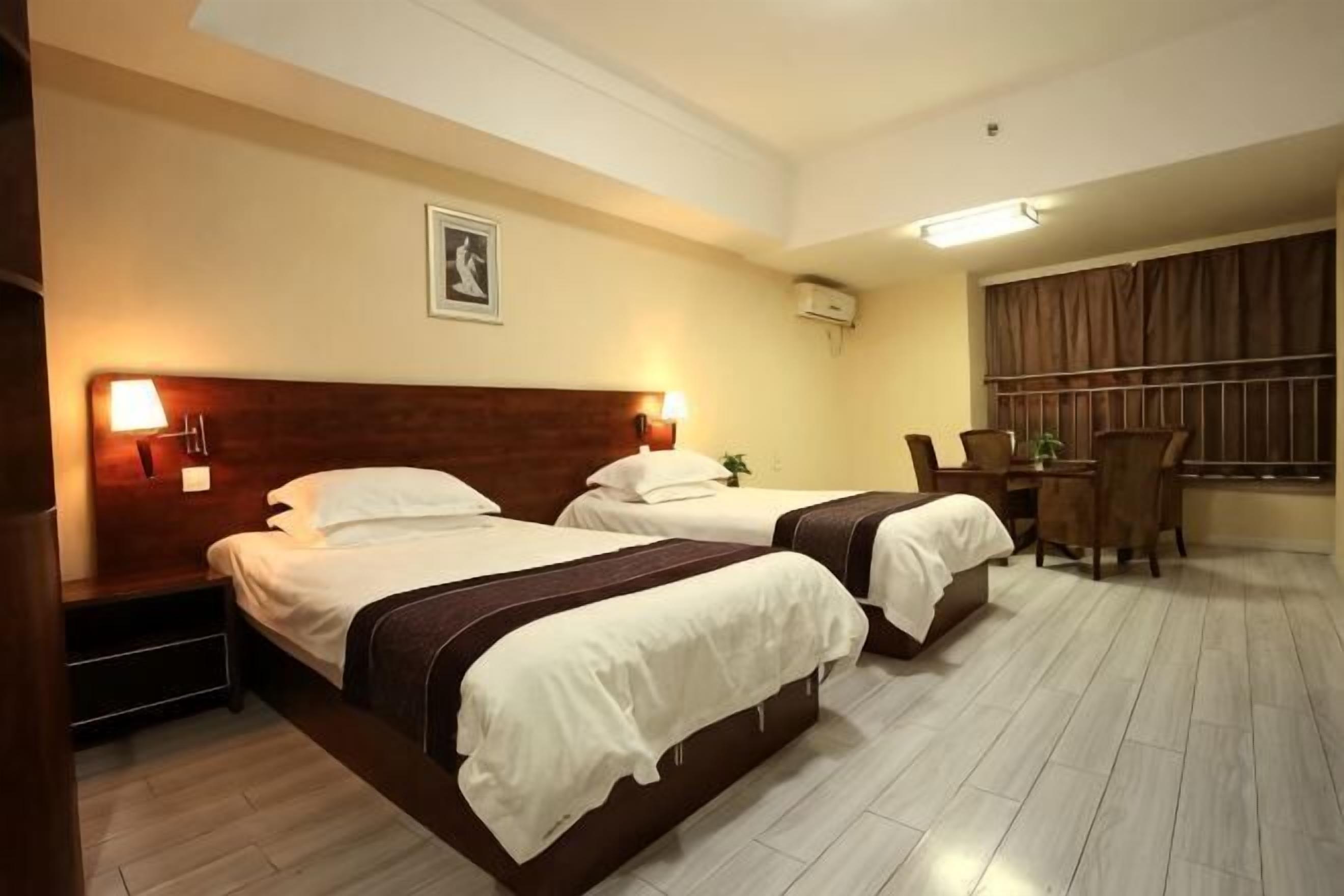 A hotel room with two beds, a desk, chairs, and a window with curtains.