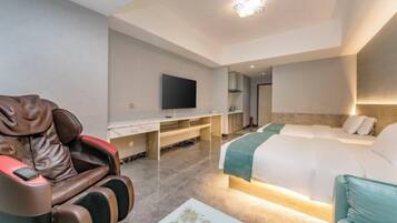 A hotel room with a massage chair, a bed, a desk with a TV, and a small table.