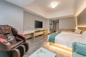 Une chambre d’hôtel équipée d’un fauteuil massant, d’un lit, d’un bureau avec une télévision et d’une petite table.