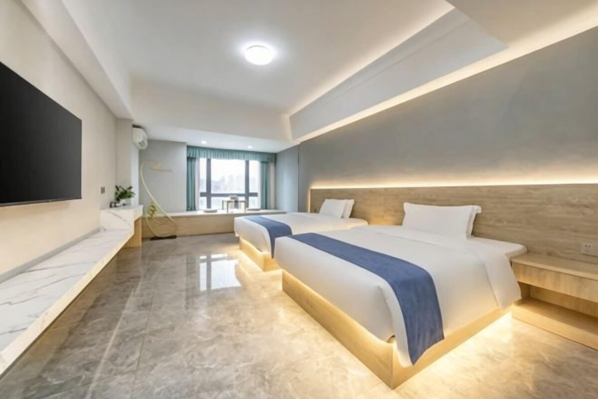 Une chambre d’hôtel moderne équipée de deux lits, d’un téléviseur à écran plat et d’une grande fenêtre.