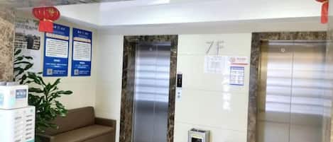 A reception area with two elevators, a sofa, a trash bin, and informational posters on the wall.
