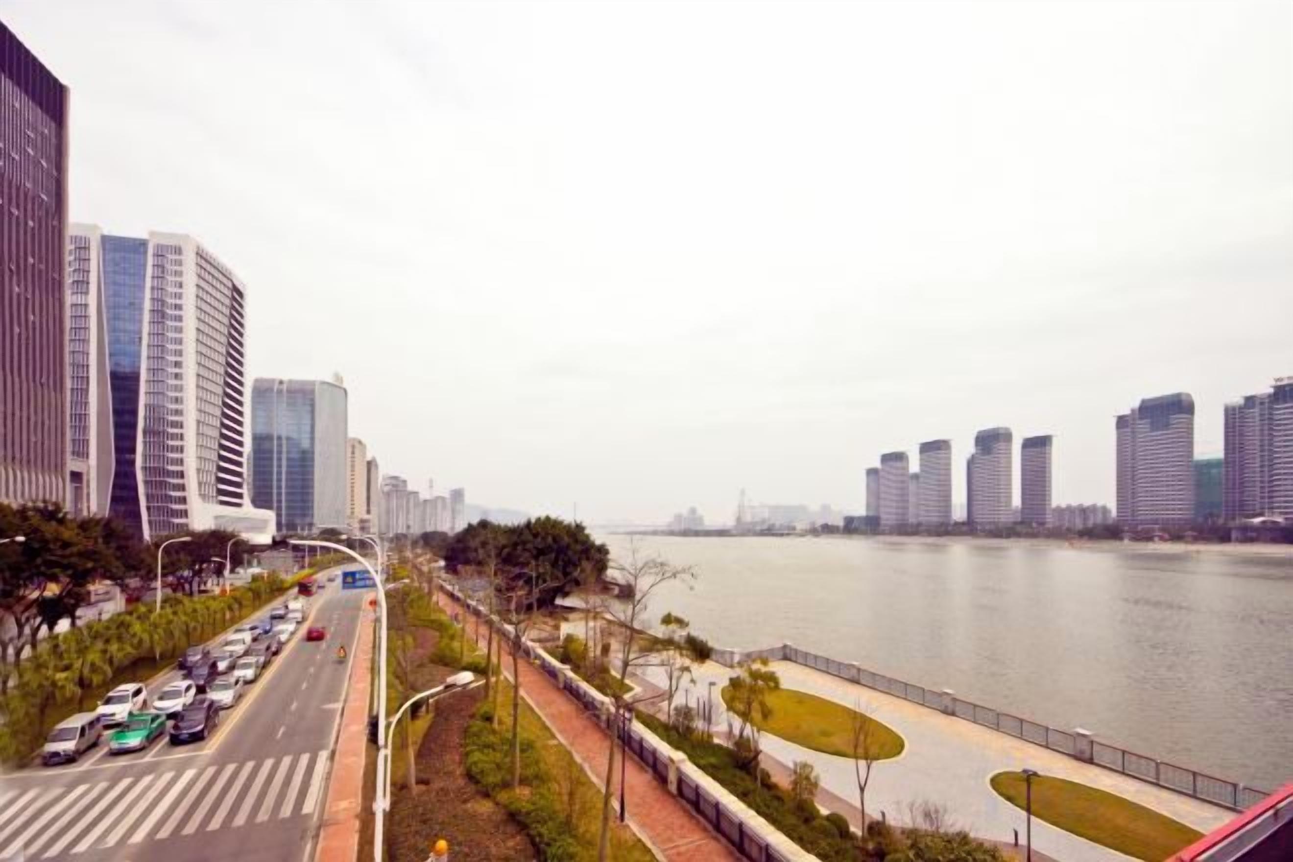 A river with buildings on one side and a road with cars on the other.