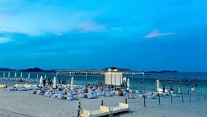 A beach with rows of sunbeds and umbrellas, a covered seating area, and a view of the sea. - Jinfan City Hotel (Fuzhou)