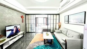 Ein modernes Wohnzimmer mit Flachbildfernseher, einer Couch, einem Couchtisch und einem gemusterten Teppich.