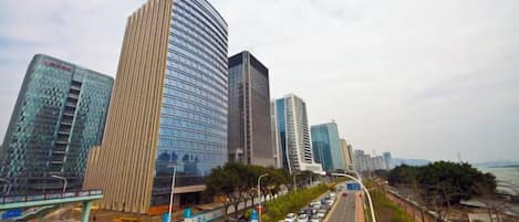 A cityscape with modern high-rise buildings, a road with vehicles, and a pedestrian walkway.