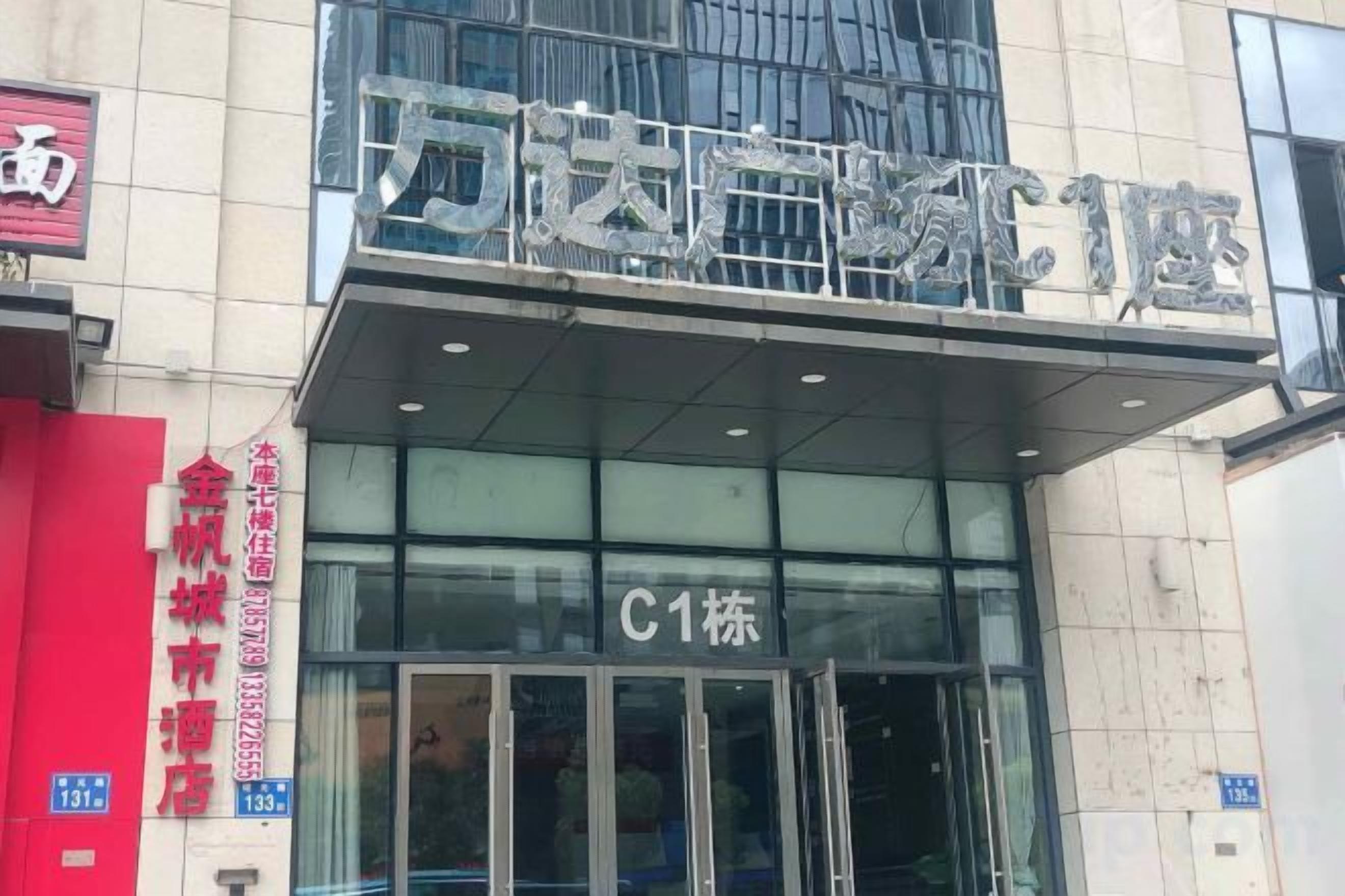 Entrada de hotel com fachada de vidro, placa indicando o número do quarto C1 e um letreiro vermelho à esquerda.