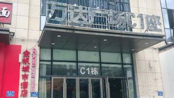 Entrada de hotel com fachada de vidro, placa indicando o número do quarto C1 e um letreiro vermelho à esquerda.